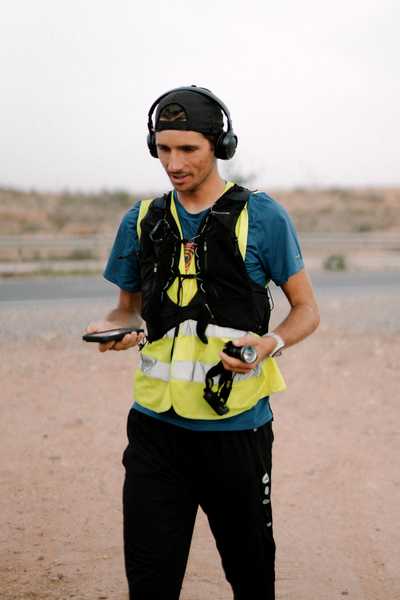 Norman Junker mit Kopfhörern und Laufweste, ein Mobiltelefon in der Hand.