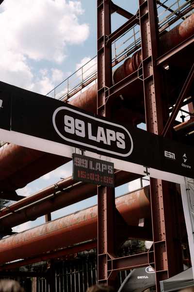 Torbogen mit dem Schriftzug 99 Laps vor einer Industriekulisse.