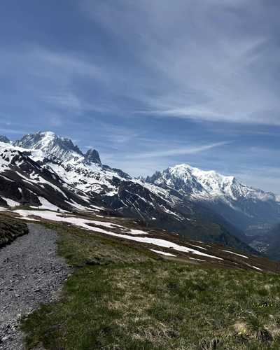 Blick von einem Bergweg über ein Tal auf schneebedeckte Gipfel.
