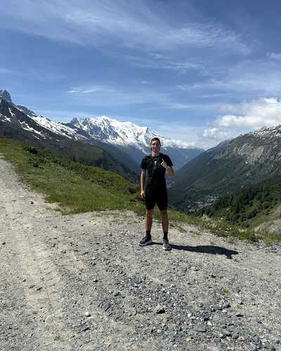 Norman Junker auf einem breiten Schotterweg vor schneebedeckten Bergen.